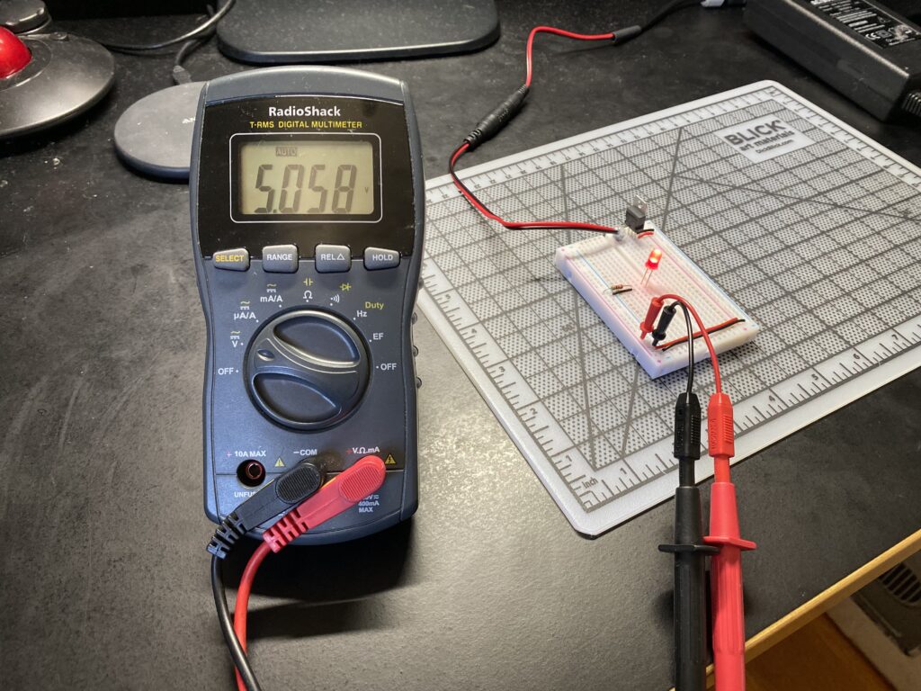 Multimeter probes reading 5.058 volts on a circuit board with red LED