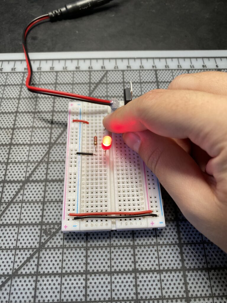 Finger pushing button on breadboard with lit red LED