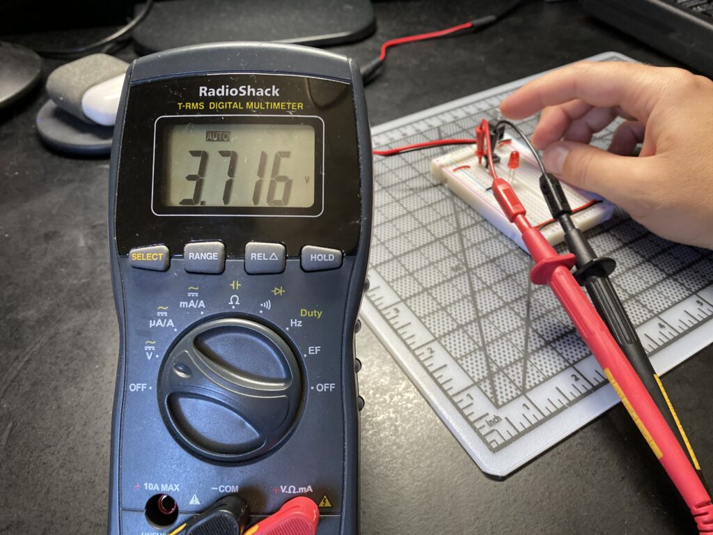 Multimeter reading 3.716 volts across a pushbutton on a breadboard